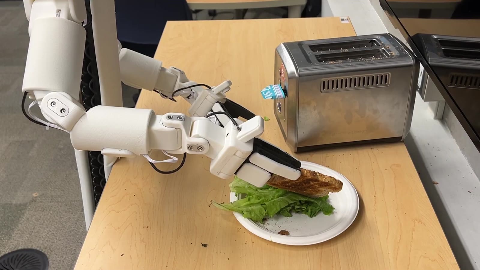 The gripper pressing the top slice onto lettuce on the plate