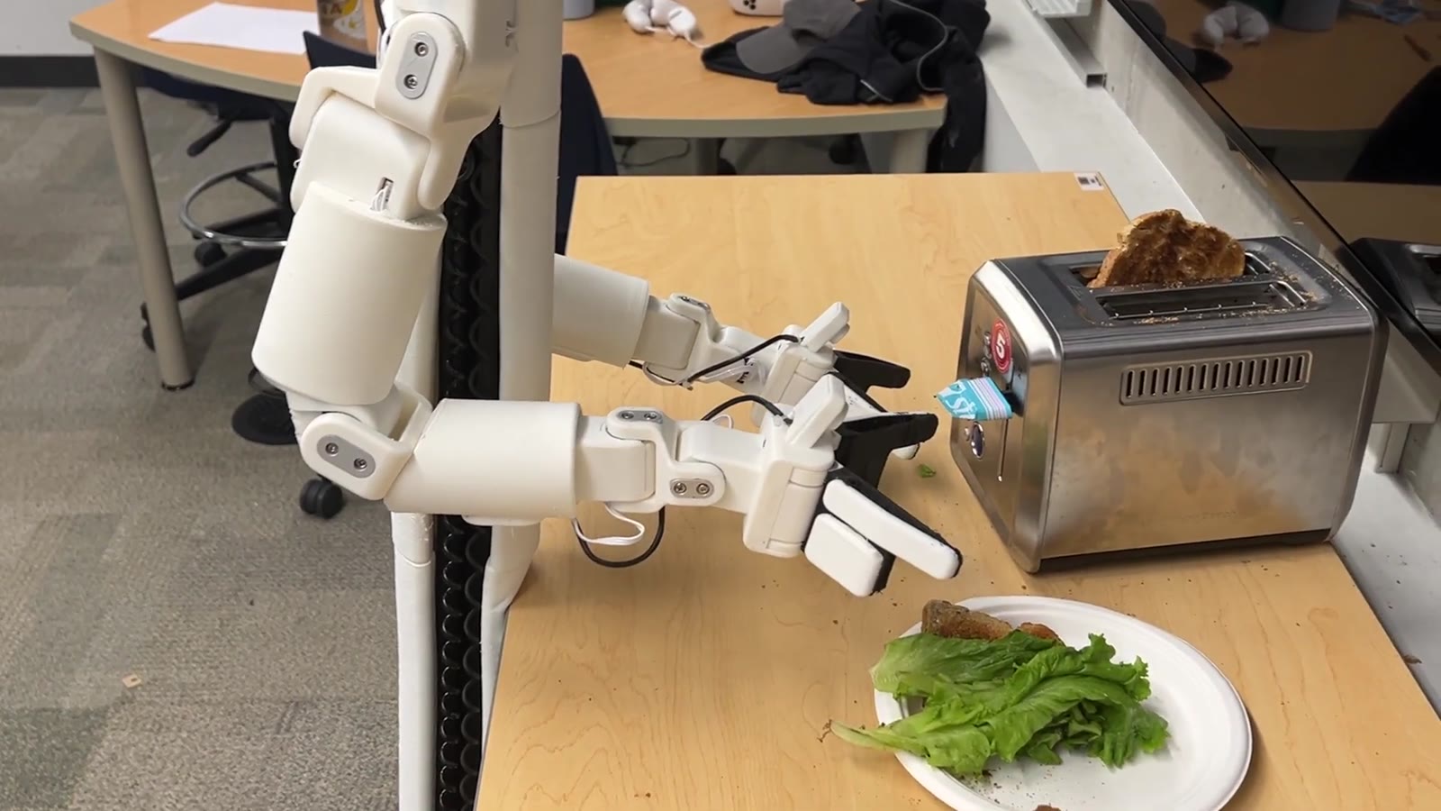 The robot placing lettuce onto the bread on the plate