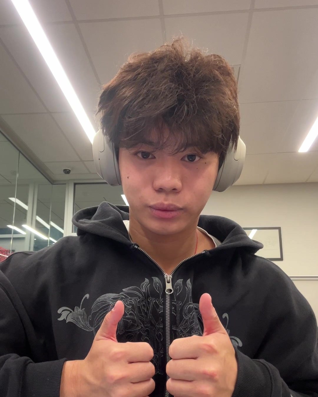 Max Yuan in headphones and a black hoodie, giving two thumbs up